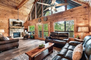 Ein geräumiges Wohnzimmer mit Kamin aus Stein, Ledersofas und einer großen Holzbalkendecke.
