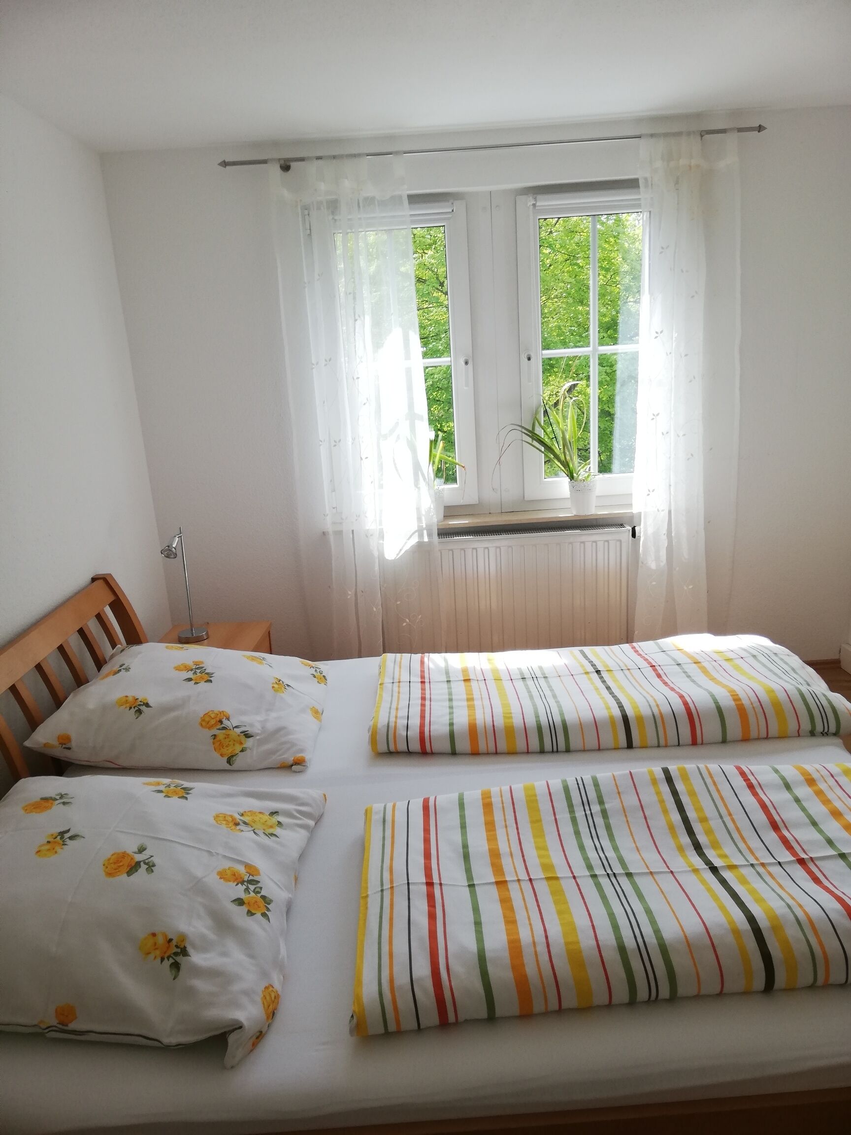 A bedroom with a bed, two pillows, a window with curtains, and a radiator.