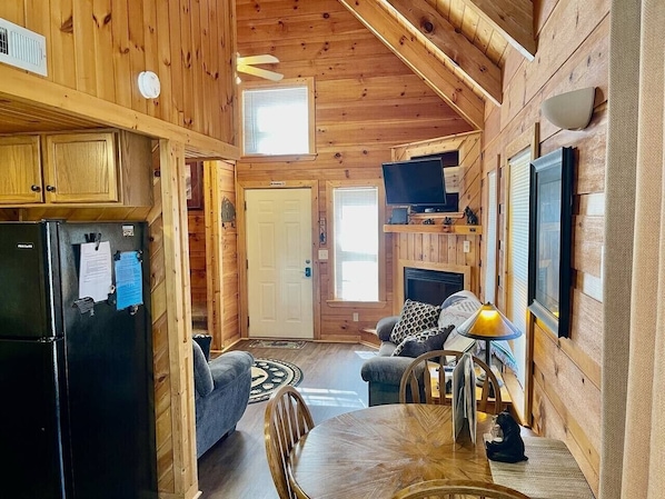 Een chaletinterieur met een keukenhoek, een zithoek met een tafel en stoelen, een open haard en een televisietoestel.