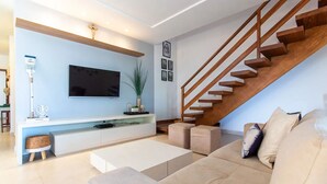 A modern living room with a wooden staircase, a flat-screen TV, and a minimalist design.
