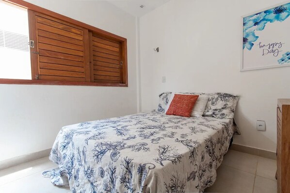A bedroom with a bed, a window with wooden shutters, and a 'happy day' artwork on the wall.