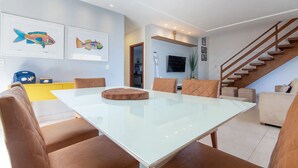 A modern living room with a glass-top dining table, brown cushioned chairs, a staircase, and a yellow accent wall.