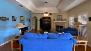 Una sala de estar con un sofá azul, una chimenea, un televisor y un ventilador de techo.