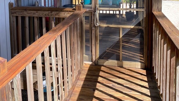 Un espacio al aire libre cubierto con piso de madera, una puerta de vidrio que da a un balcón y vista a un edificio con barandal de madera.