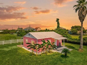 A pink house with a porch and a white fence in a grassy area.