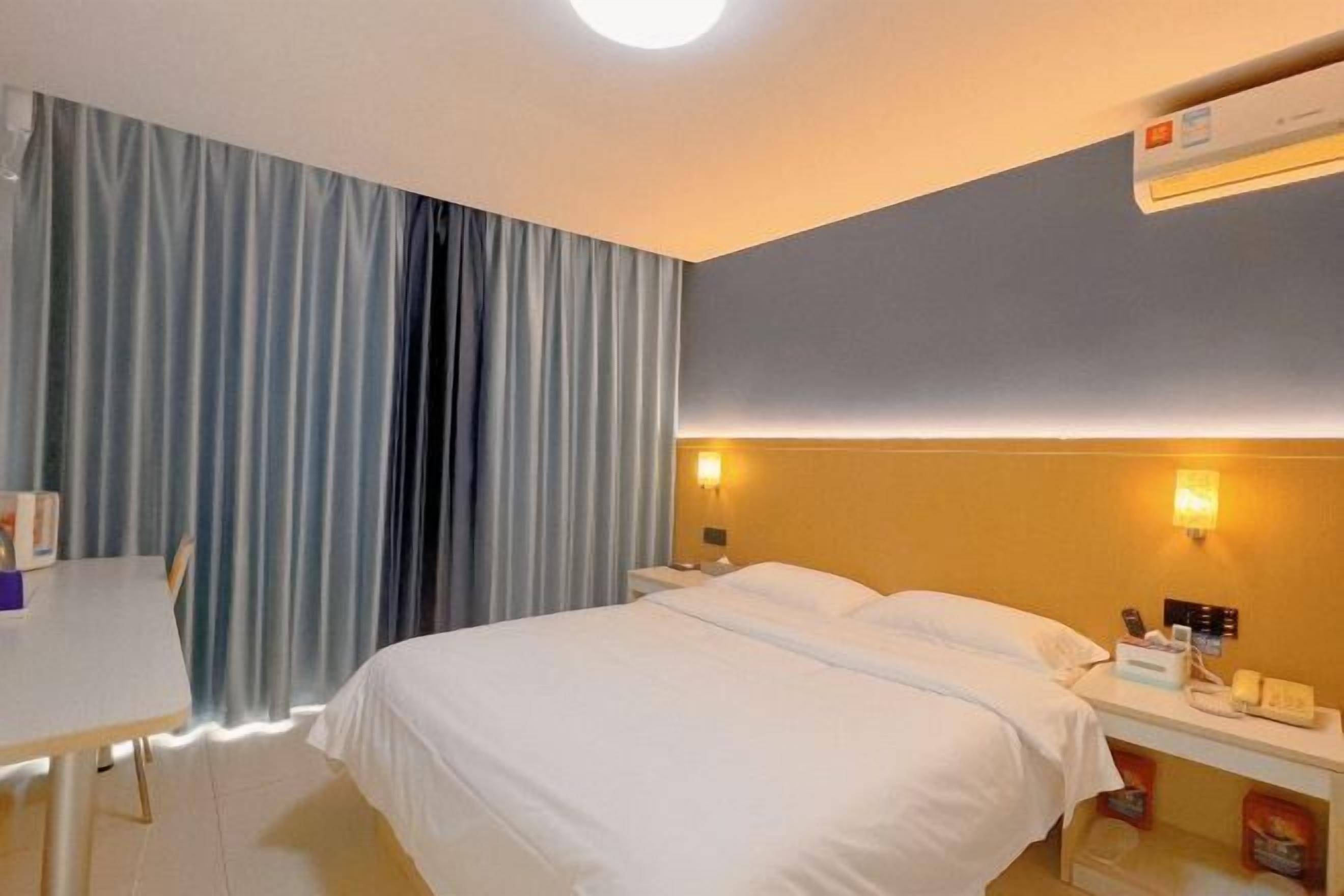 A hotel room with a bed, bedside table, and a desk with a chair.