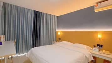 A hotel room with a bed, bedside table, and a desk with a chair.