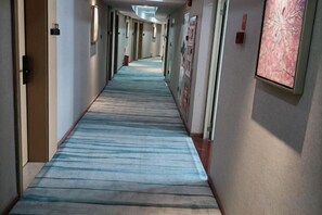 A long hallway with a patterned carpet, doors on the left, and framed artwork on the right. - Liudianban Inn (Dongguan Nancheng Xiping) (Dongguan)
