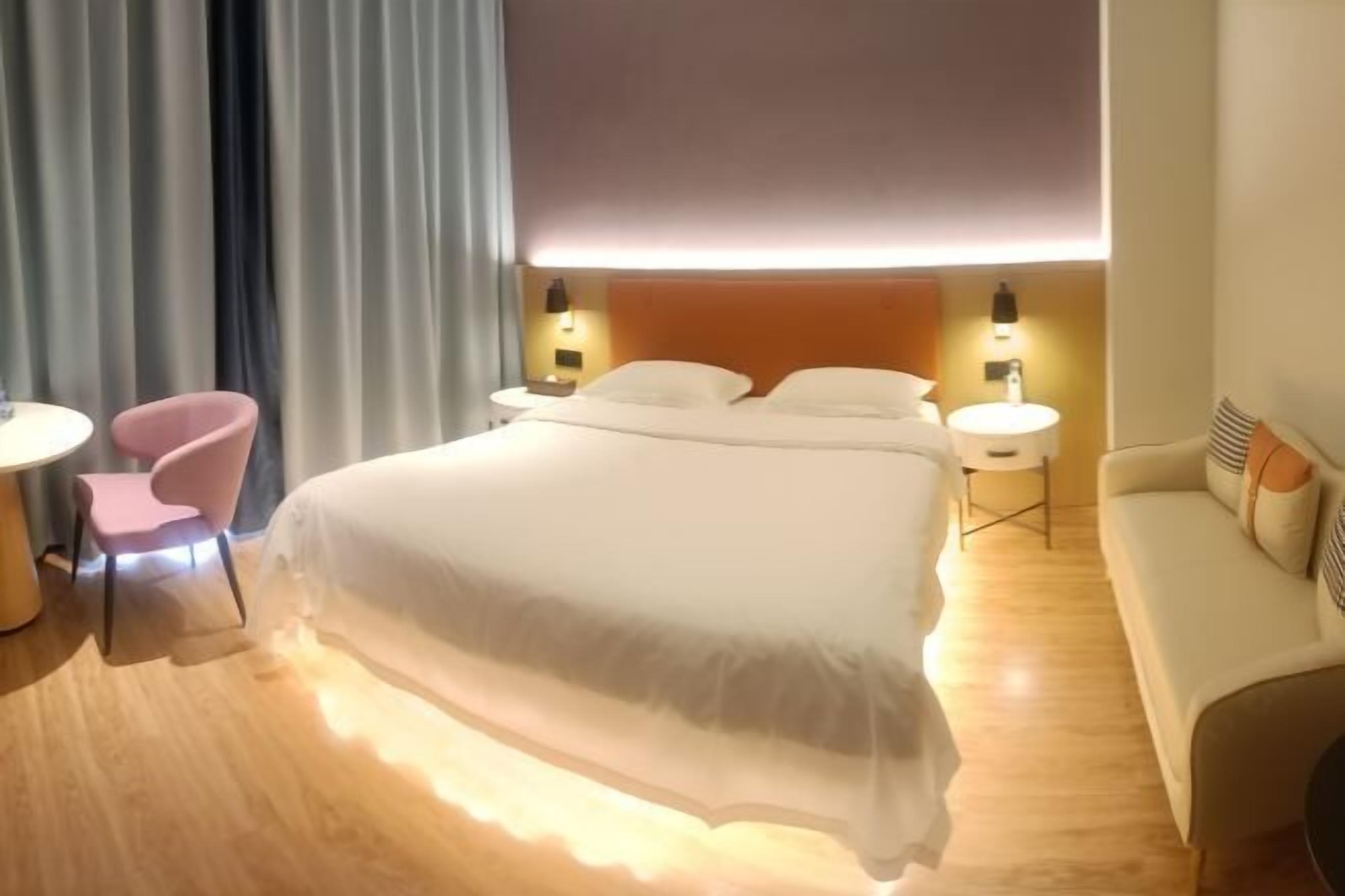A hotel room with a bed, bedside tables, a chair, a sofa, and a curtain.