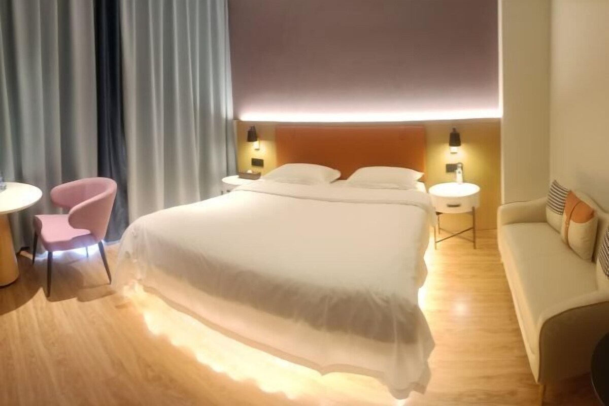 A hotel room with a bed, bedside tables, a chair, a sofa, and a curtain.
