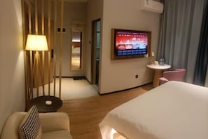 A hotel room with a bed, a TV, a desk, a chair, and a lamp.