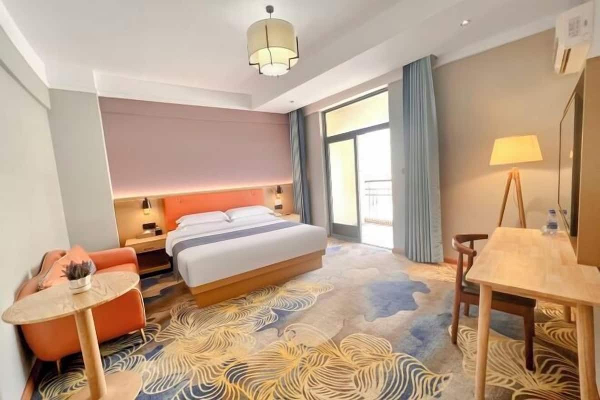 Une chambre d’hôtel comprenant un lit, un bureau, une chaise, une petite table, une lampe et une vue sur l’extérieur.