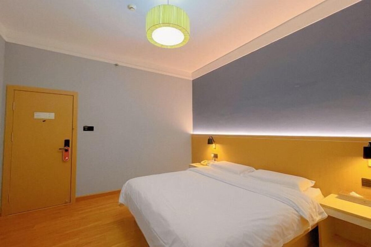 A hotel room with a bed, a bedside table, a lamp, and a door.