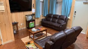 Una sala de estar con un sofá de cuero marrón, una mesa de centro, un televisor y una ventana con cortinas azules.