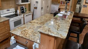 Una cocina con armarios de madera, encimera de granito, microondas, estufa, lavavajillas y refrigerador.