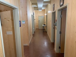 A wooden-paneled hallway with doors on both sides, a sign indicating a trance, and a small table in the distance.
