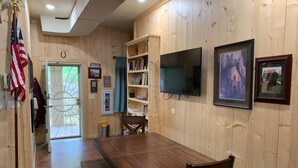 Una habitación con paneles de madera, una mesa de comedor de madera, sillas, un televisor y estanterías con libros y adornos.