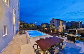 Terraza con piscina, mesa y sillas, una parrilla y vistas de edificios circundantes.