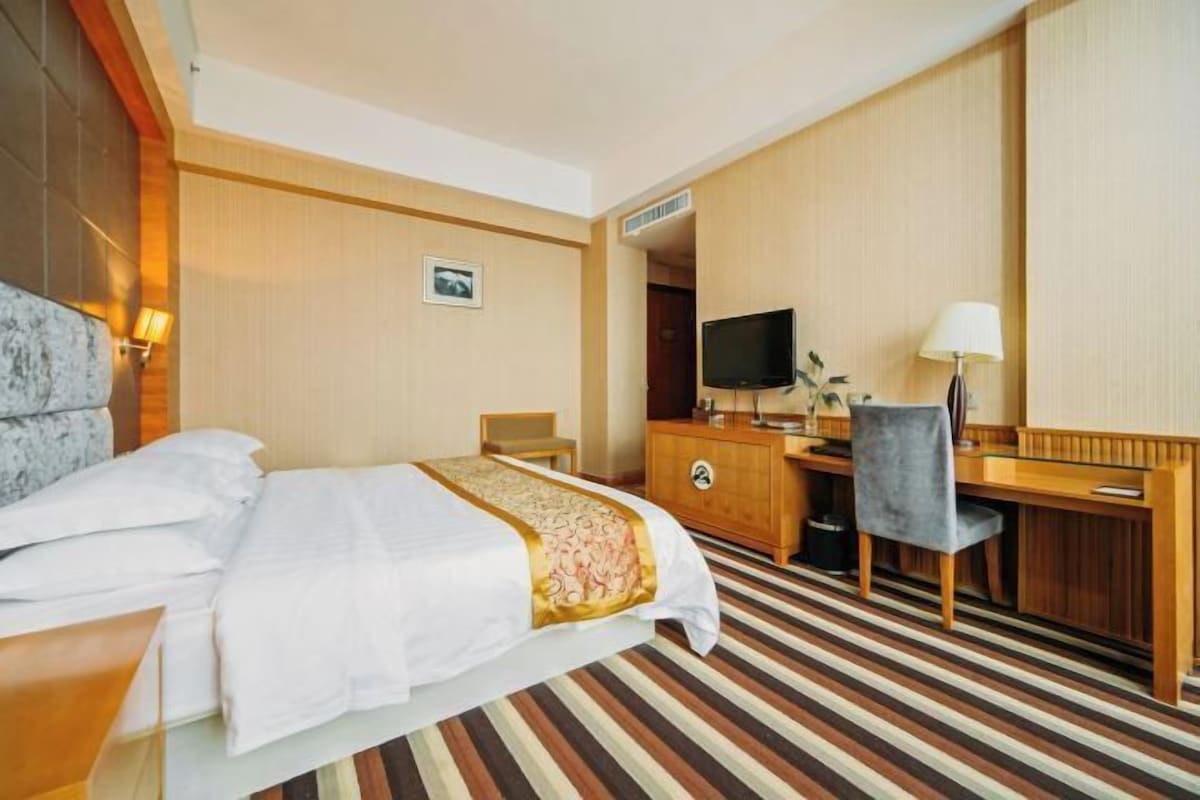 A hotel room with a bed, a desk, a chair, a television, and a lamp.