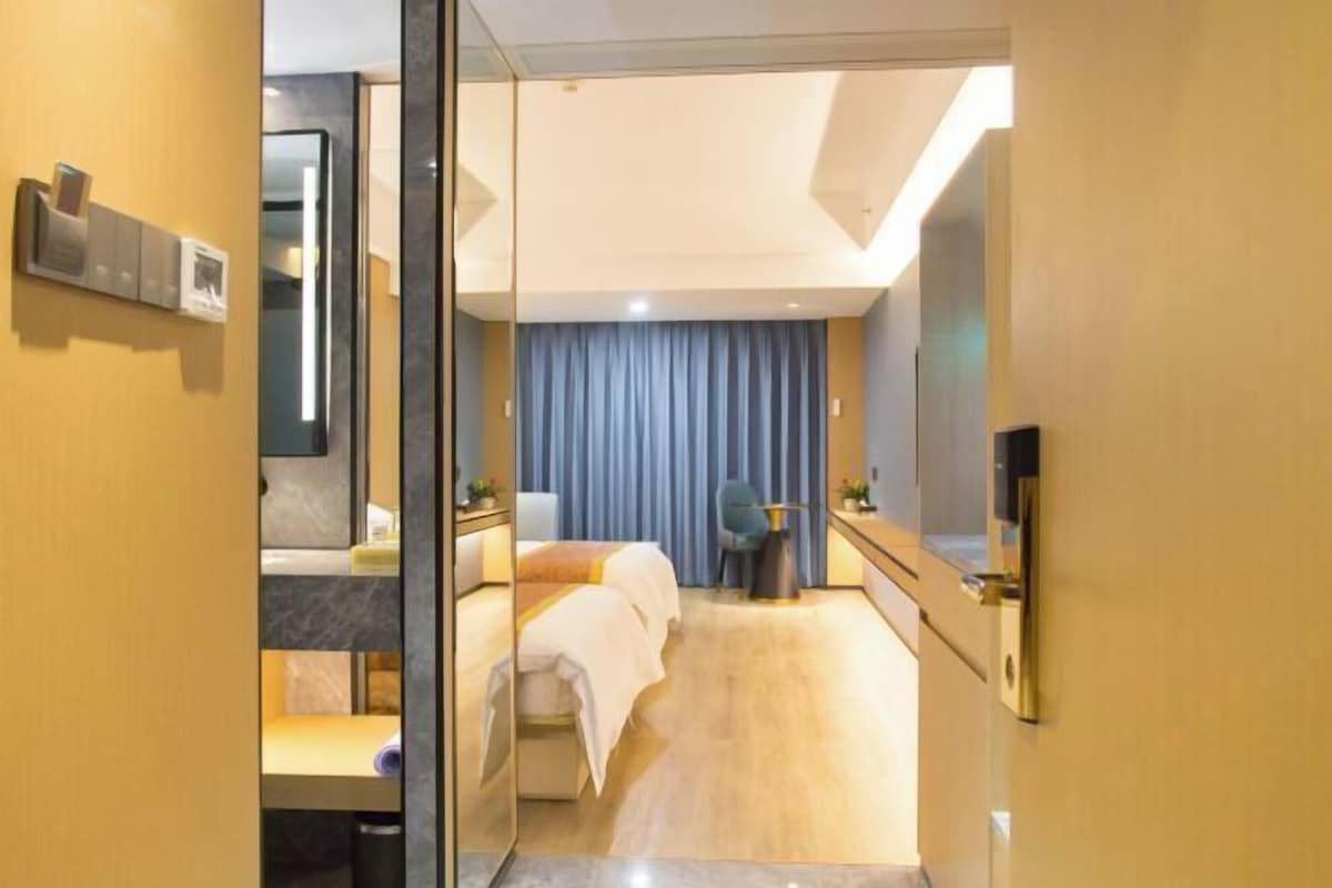 A hotel room with a bed, a desk, a chair, a mirror, and a TV.