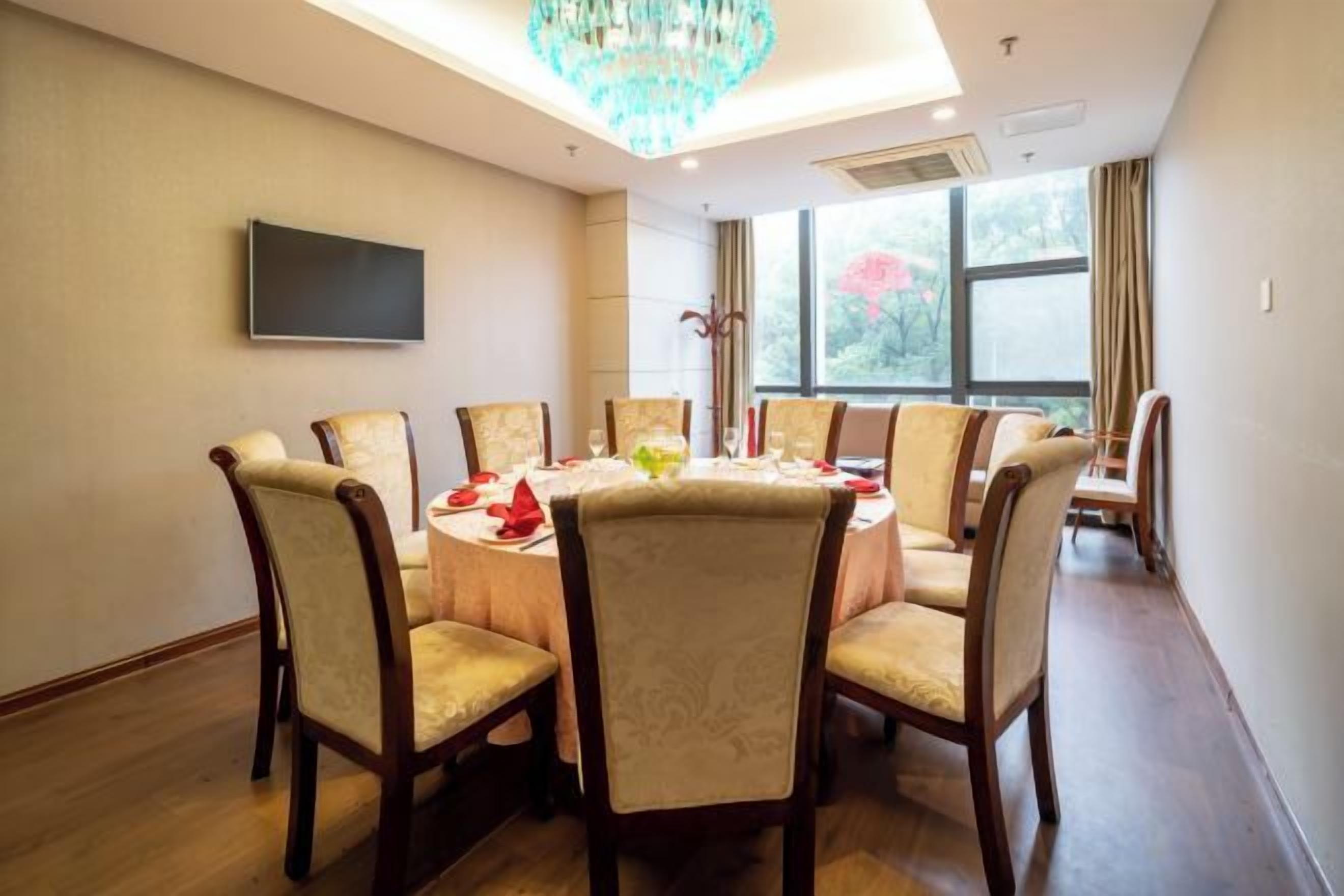 A conference room with a round table, chairs, a flat-screen TV, and a large window with curtains.