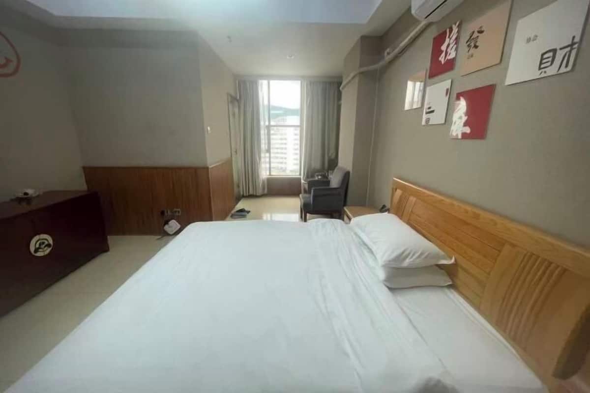 Habitación de hotel con una cama grande, cabecera de madera, escritorio con silla y ventana con cortinas.