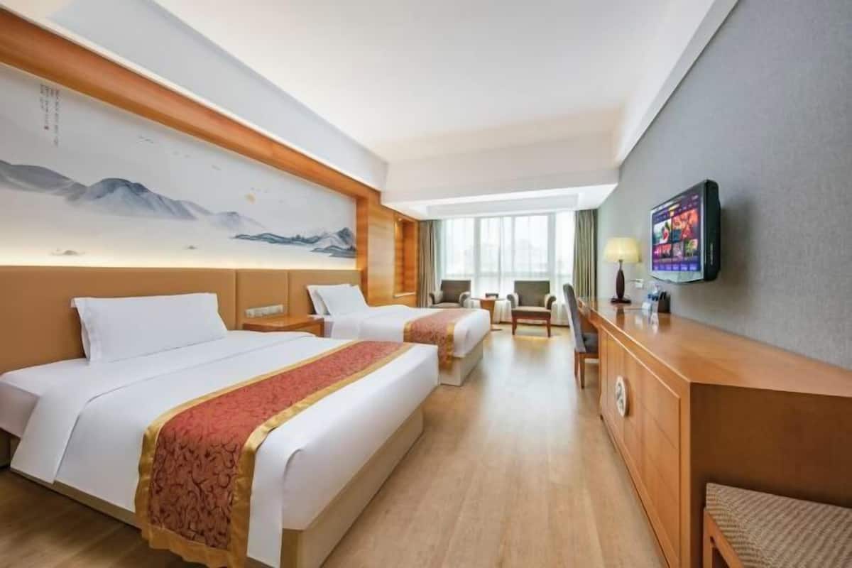 Habitación de hotel con dos camas, un escritorio, un televisor y un cuadro grande en la pared.