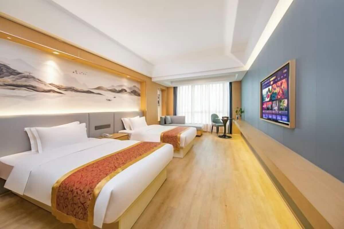 Habitación de hotel con dos camas, un escritorio, una silla, un televisor y un cuadro en la pared.