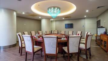 A dining area with a round table surrounded by chairs, a chandelier, and a television on the wall.