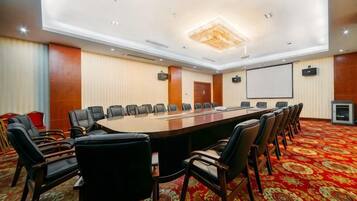 A conference room with a long table, multiple chairs, a projector screen, and a carpeted floor.
