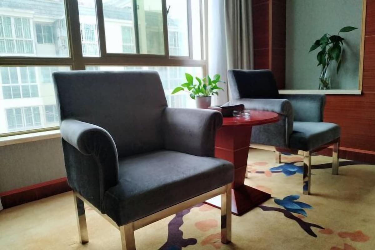 A modern room with a large window, a dark grey armchair, a smaller armchair, a small round table, and a potted plant.