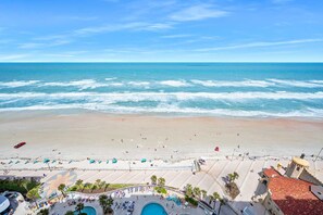 Un complejo turístico en la playa con zona de piscina, sombrillas y vistas al océano.