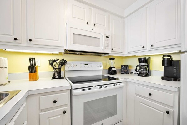 A modern kitchen with white cabinets, a microwave, stove, and coffee maker.