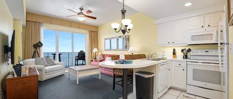 A hotel room with a balcony, a dining area, a kitchen, and a living room.