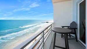 Un balcón con vistas a la playa y al océano, una mesa y dos sillas.