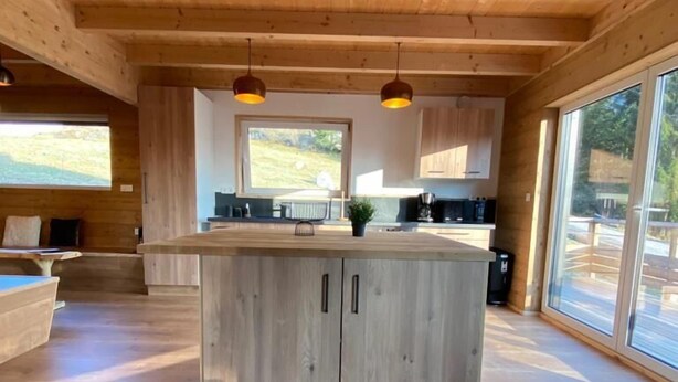 Une cuisine spacieuse dotée de meubles en bois et d’un îlot central, ainsi que de grandes fenêtres offrant une vue sur l’extérieur.