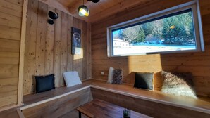 L’intérieur chaleureux d’un chalet, avec ses murs en bois, un banc et une grande fenêtre donnant sur un paysage enneigé.