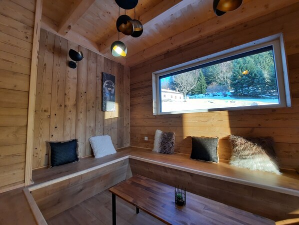 A cozy cabin interior with wooden walls, a bench, and a large window offering a view of a snowy landscape.