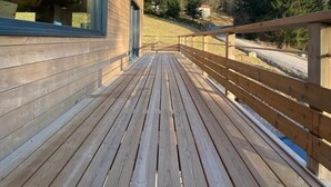 Une terrasse en bois mène à un bâtiment doté de grandes fenêtres et offrant une vue sur une zone boisée.