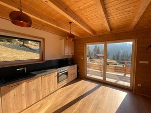 A modern kitchen with wooden cabinets, a black countertop, and a large window offering a view of a mountainous landscape.