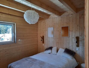 A wooden cabin bedroom with a bed, a hanging light fixture, and framed pictures on the wall.