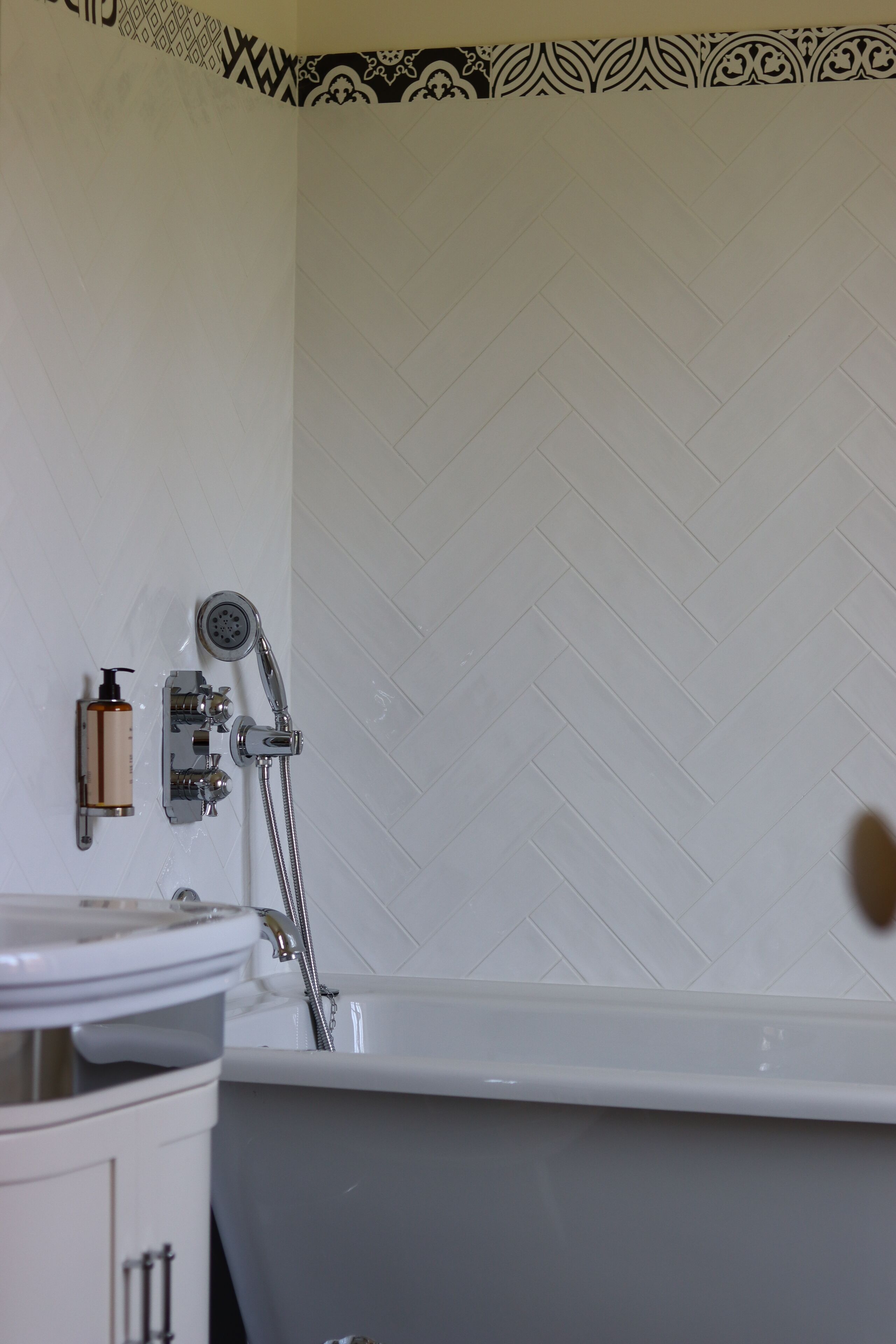 A bathroom with a white bathtub, a showerhead, and a bottle of shampoo on the wall.