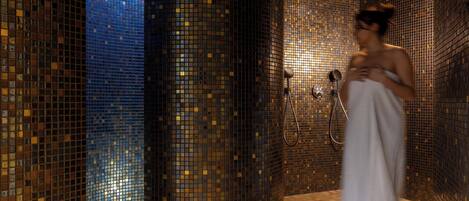 A tiled bathroom with a shower area and a person standing in the shower.