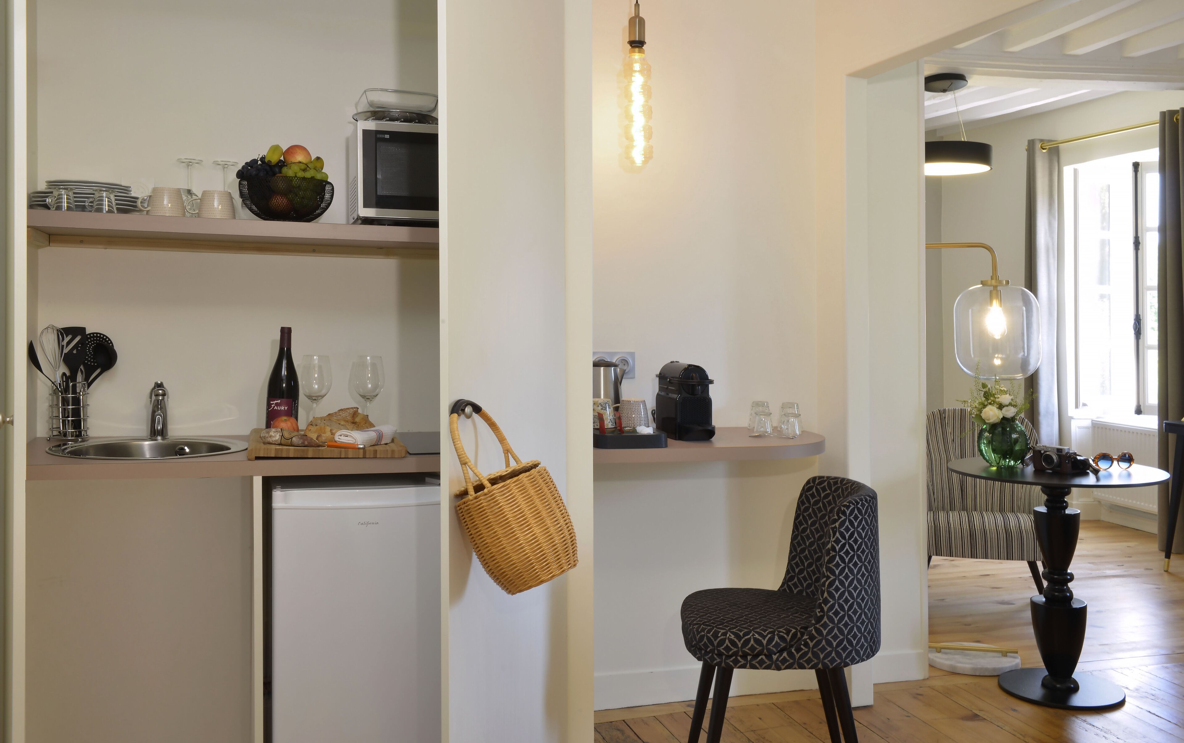 A modern kitchen with a microwave, sink, and various kitchen items. There is a wicker basket hanging on the wall and a chair in the dining area.