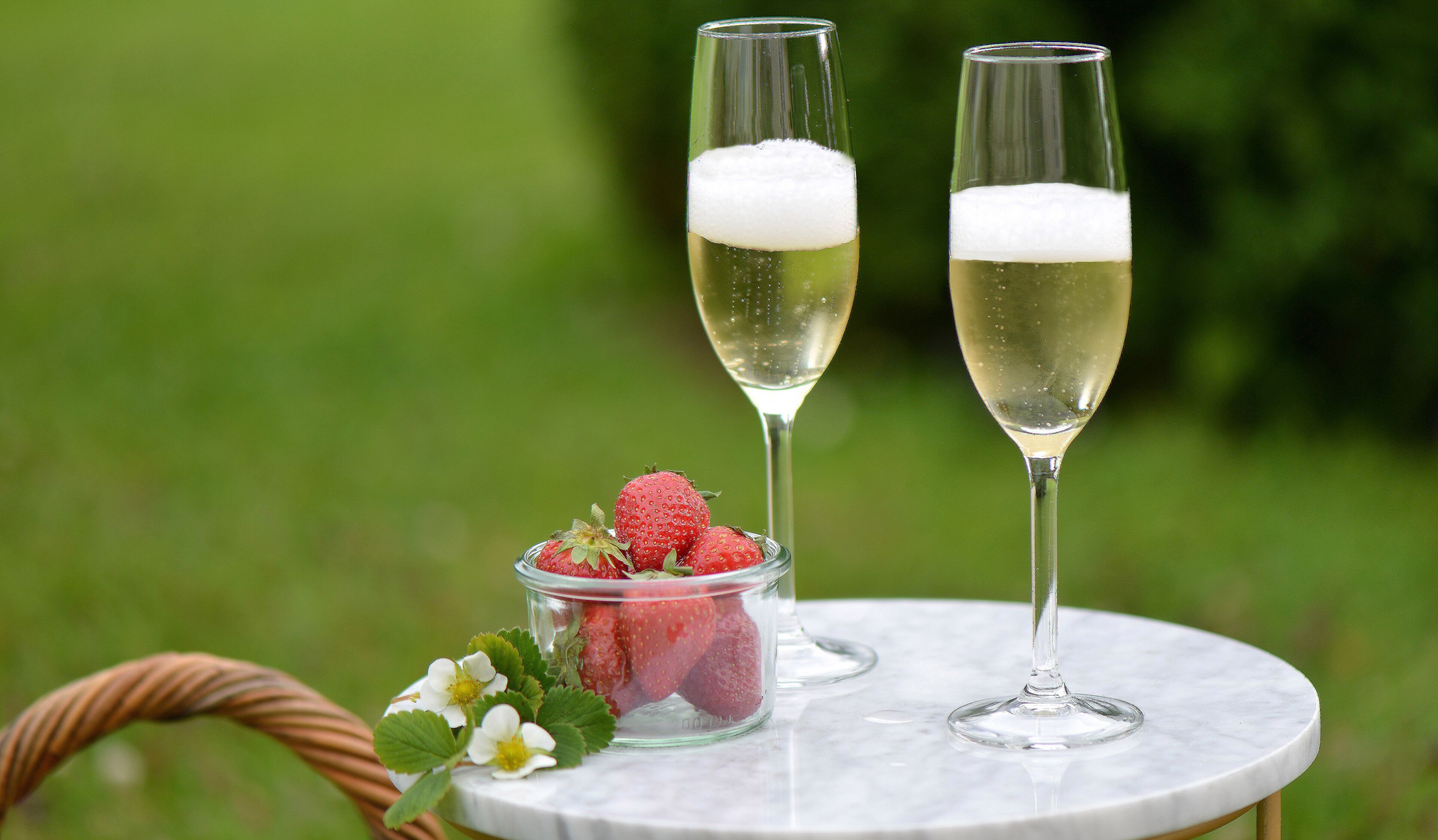 Two champagne glasses on a marble table with strawberries and a small bowl of strawberries.