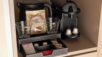 A coffee station with a coffee maker, a glass carafe, a bag of biscuits, and a compartment with coffee pods and a box of tea.