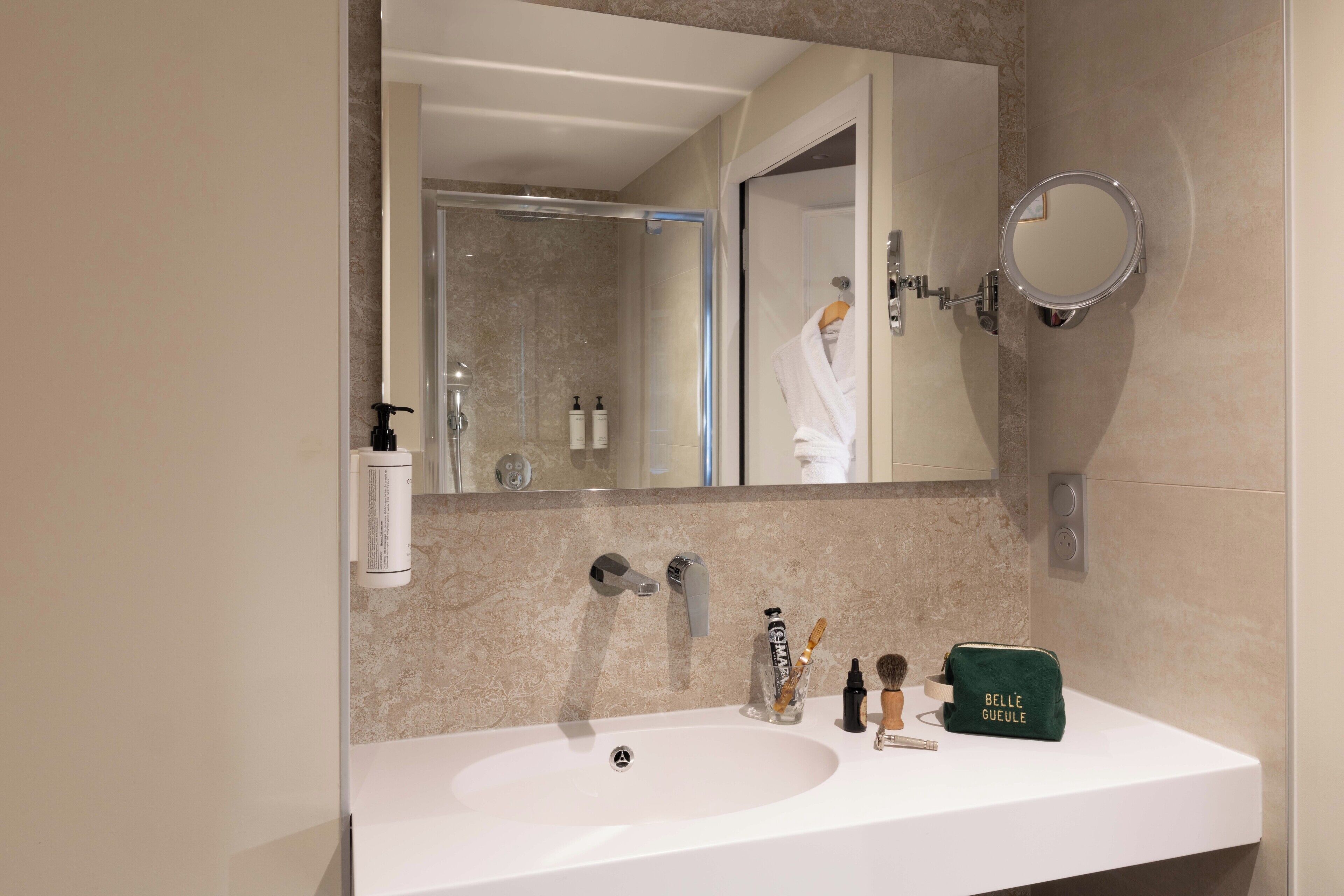 Un baño con un lavabo blanco, dos grifos, un espejo y artículos de aseo en la encimera.