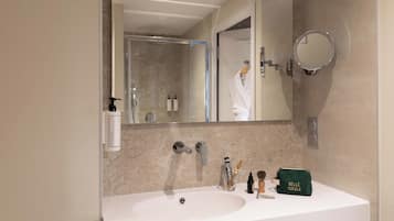 Un baño con un lavabo blanco, dos grifos, un espejo y artículos de aseo en la encimera.
