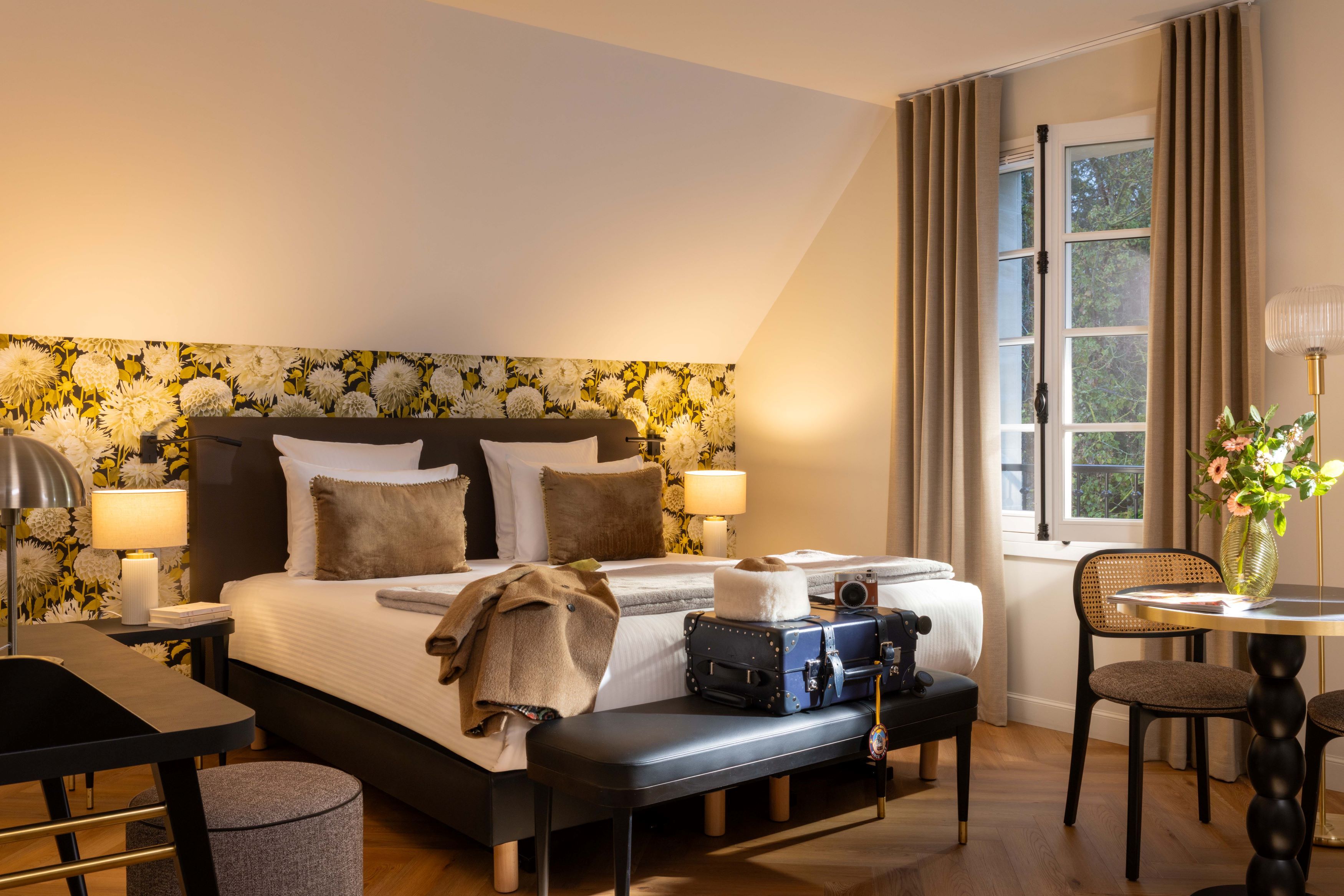 Une chambre d’hôtel avec un grand lit, un bureau, une chaise, une table et une fenêtre avec des rideaux.