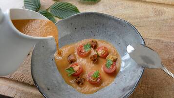 A bowl of soup with tomatoes and herbs on a wooden table.
